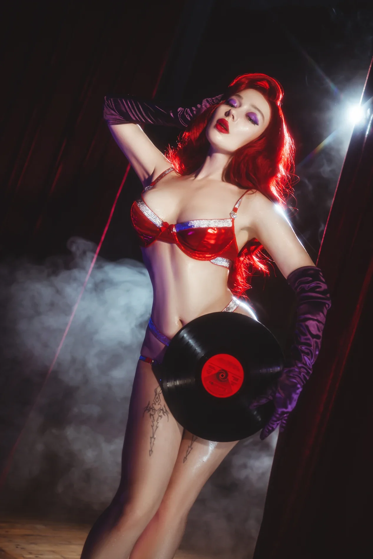 Irabyb as Jessica Rabbit in a red two-piece costume, purple gloves and theatrical light, holding a vinyl record
